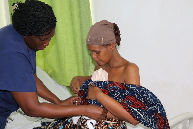 mother holding newborn assisted by clinical staff